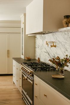 a kitchen with marble counter tops and white cabinets, gold pulls on the door handles