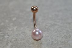 a gold nose piercing with a pink pearl on it's end, sitting on a gray surface