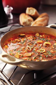 a pan filled with pasta and sauce sitting on top of a stove next to bread