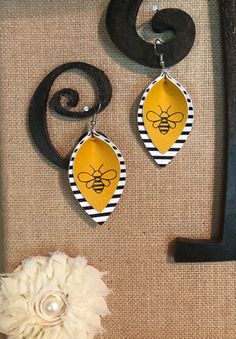 a pair of yellow and black earrings with a bee on the front hanging from it