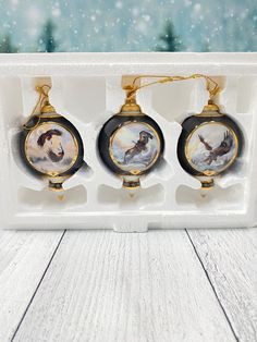 three christmas ornaments in an egg box on a white wooden table with snowflakes