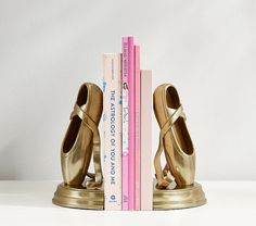 a pair of gold ballet shoes sitting on top of a bookend next to two books