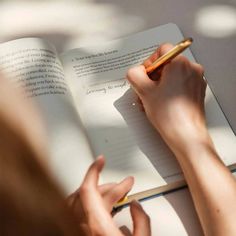 a person writing on a book with a pen in their hand and an open notebook next to them