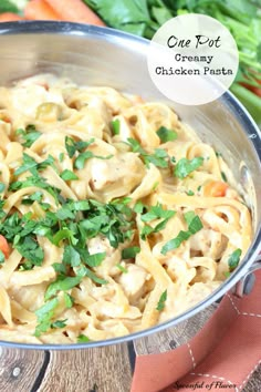 a bowl filled with chicken pasta and parsley on top of a wooden table next to carrots