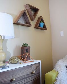 three wooden shelves on the wall above a dresser with a lamp and other items sitting on it