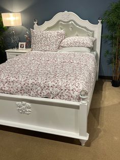 a white bed with red flowers on it in a blue walled room next to potted plants