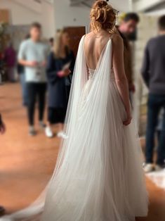 a woman in a white wedding dress is looking down at the floor while people are standing around