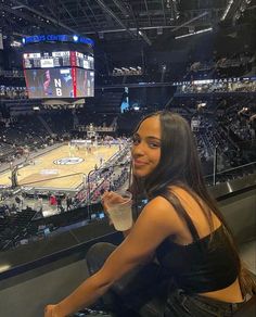 a woman sitting in front of a basketball court holding a drink