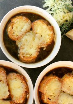 three bowls filled with food sitting on top of a table next to bread and vegetables