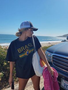 a woman is walking down the beach with her hand in her pocket and holding a pink bag