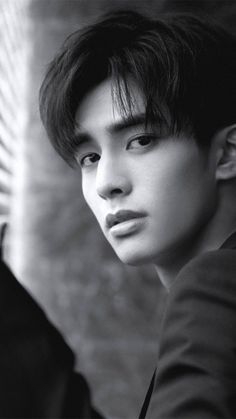 black and white photo of a young man with short hair looking at the camera while leaning against a wall