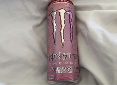 a pink monster energy drink sitting on top of a bed