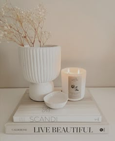 two books and a candle are sitting on top of each other in front of a white vase