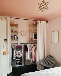 a bedroom with a bed, chair and shelves filled with clothes on hangers next to a window