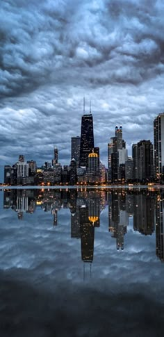 a city skyline is reflected in the water at night with dark clouds and blue sky