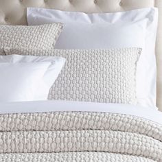 a bed with white linens and pillows on top of it, in front of a beige headboard