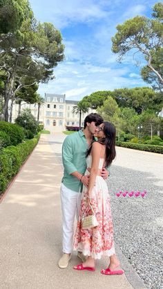 a man and woman are kissing in front of a large building with trees on the other side