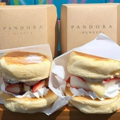 two sandwiches with cheese and strawberries in paper wrappers next to boxes on a table