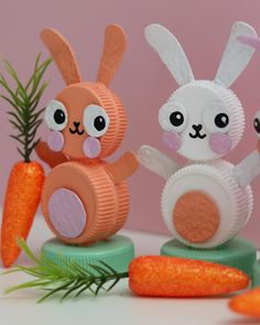 two paper rabbits sitting on top of carrots