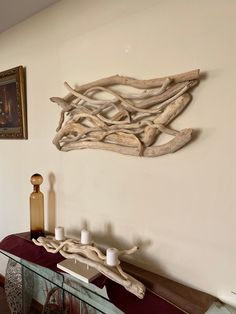 a table with candles and driftwood on it in front of a wall hanging art piece