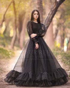 a woman in a black dress standing on a dirt road