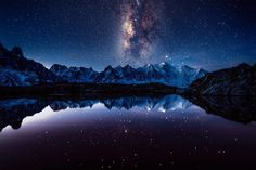 the night sky is reflected in water with mountains and stars above it, as well as an illuminated mountain range