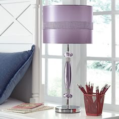 a purple lamp sitting on top of a white table next to a basket filled with pencils