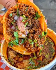 a close up of a bowl of food with meat and vegetables on top, sitting on a checkered table cloth