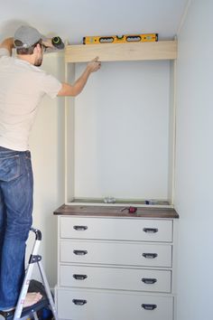 a man is standing on a ladder in the corner of a room with white drawers