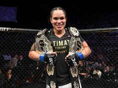 a woman standing in front of a cage holding two boxing gloves on her hands and smiling at the camera