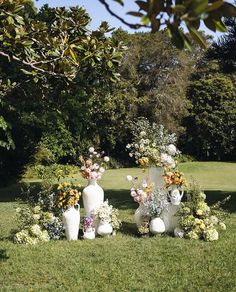 three white vases with flowers in them on the grass