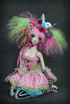 a doll is sitting on the ground wearing a pink dress with green hair and flowers in her hair