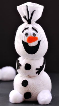 a knitted snowman sitting on top of two white balls with black dots and an orange nose