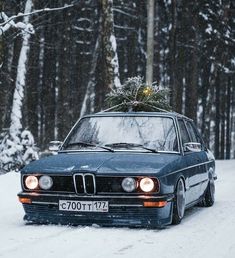 an old car with a christmas tree on the hood driving down a snow covered road