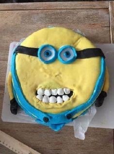 a cake with yellow frosting and blue decorations on it's face is decorated like a minion