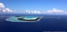 an island in the middle of the ocean under a blue sky with clouds and water