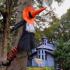 a scarecrow doll hanging from a tree in front of a blue house with orange and black striped socks