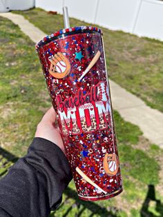 a person holding up a red glitter tumbler with baseballs and bats on it