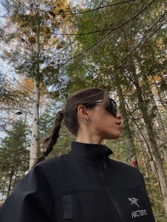 a woman standing in the woods with her hair pulled back and sunglasses on, looking off into the distance