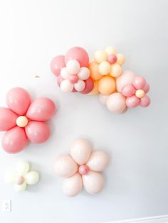 three balloons are arranged in the shape of flowers on a white wall, and one balloon is shaped like a flower