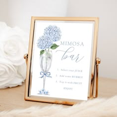 a blue hydrangea flower is in a glass vase on a table next to a sign that says mimosa bar