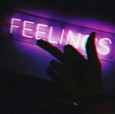 a person holding their hand up in front of a neon sign that reads feelin's