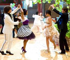 several people dancing on a dance floor in front of a group of people wearing dresses and tuxedos