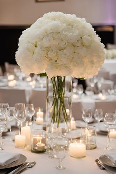 a vase filled with white flowers sitting on top of a table next to glasses and candles