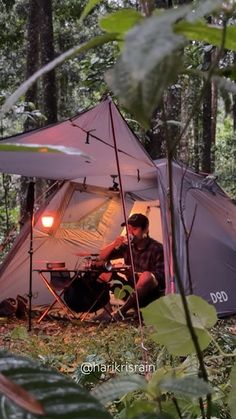 a man sitting in the woods next to a tent