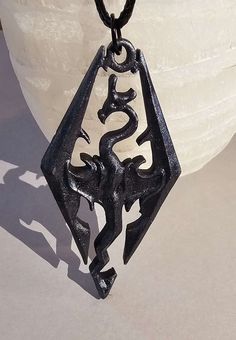 a black pendant with an ornate design hanging from it's side on a white surface