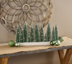 christmas decorations on a table in front of a circular metal wall decoration with trees and balls