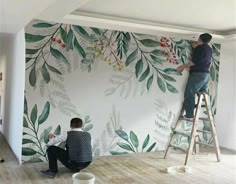 two men painting a wall with green leaves and berries on it, while another man sits on a ladder