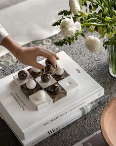 a person is playing chess on a table with flowers in the vase and books nearby