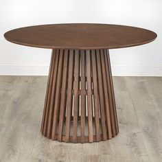 a round wooden table sitting on top of a hard wood floor covered in white walls